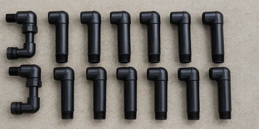 Ten black PVC swing joint sprinkler fittings arranged in two rows on a light gray concrete surface, showing threaded ends and elbow joints.