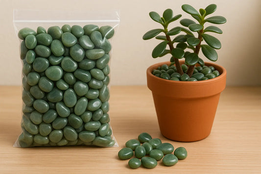 A clear bag of smooth green jade pebbles beside a terracotta pot with a jade plant, all placed on a light wooden surface indoors.